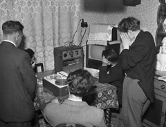 Black and white photo of people gathered around an old radio